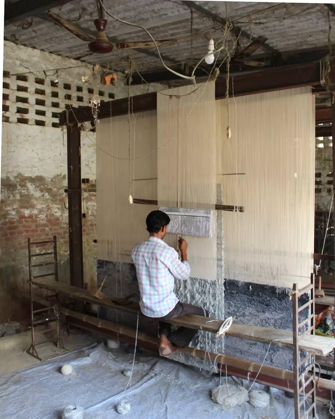 Weavers at vertical looms hand-knotting a rug
